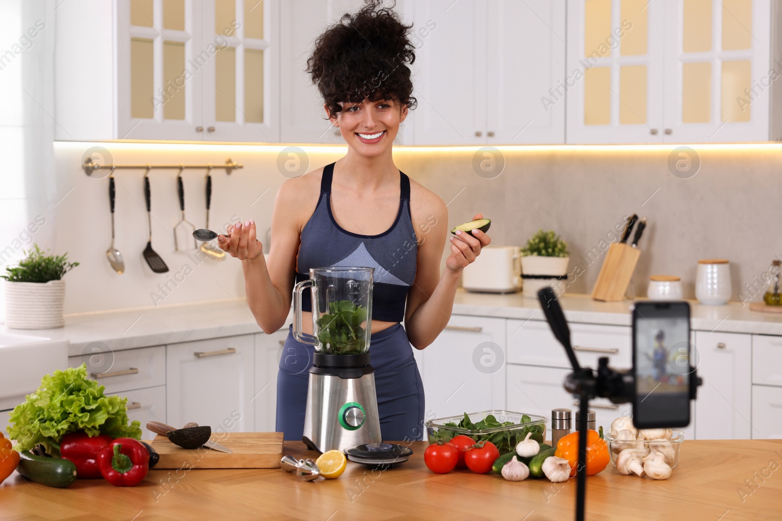 Photo of Smiling food blogger cooking while recording video in kitchen