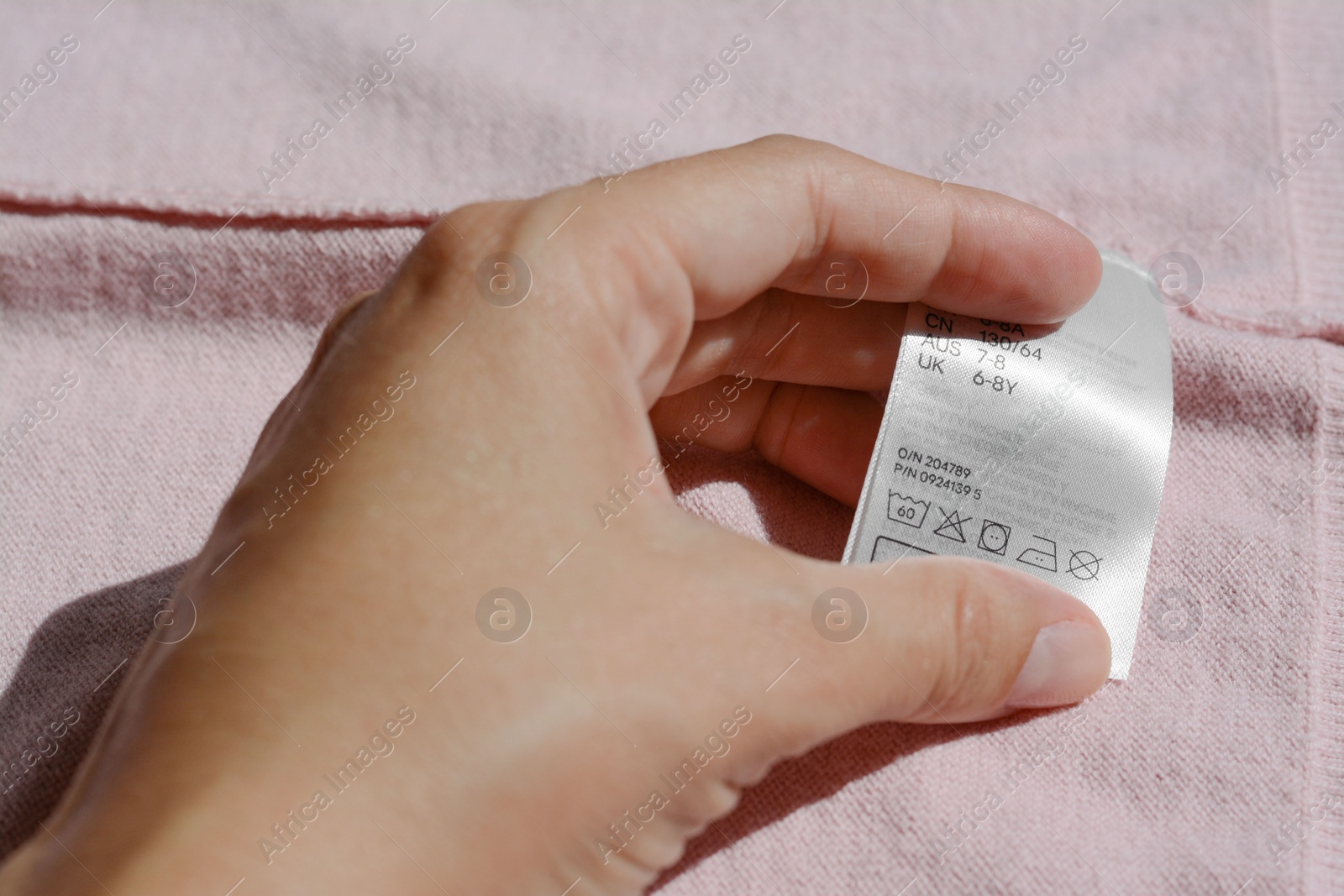 Photo of Woman holding clothing label on pale pink garment, closeup