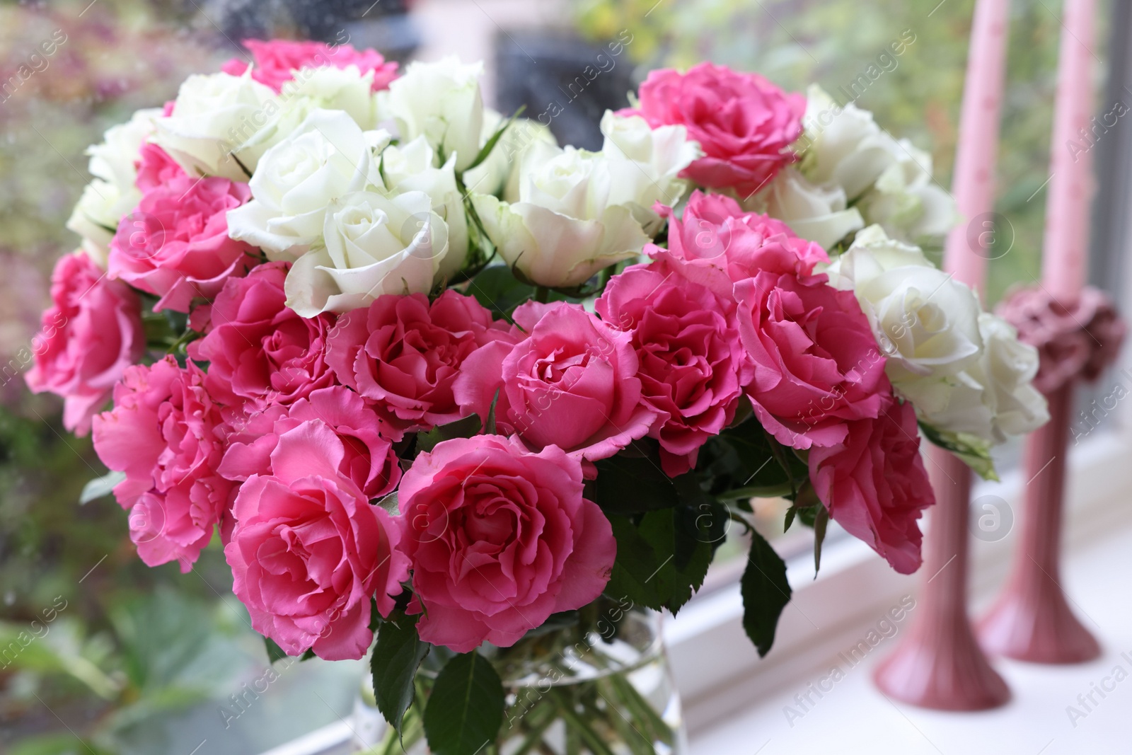 Photo of Vase with beautiful bouquet of roses and candles on windowsill indoors, closeup