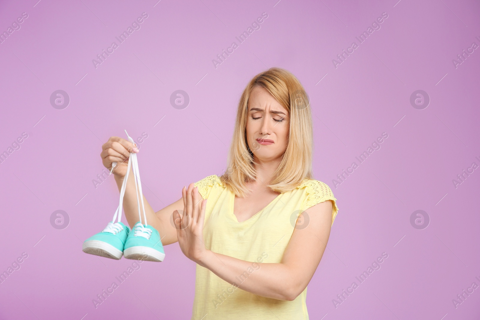 Photo of Young woman with stinky shoes on color background. Air freshener