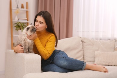Photo of Woman kissing her cute cat on comfortable sofa at home