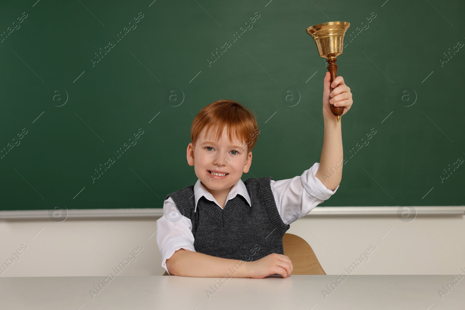 Photo of Cute little boy ringing school bell in classroom