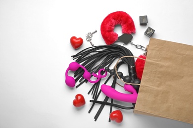 Paper shopping bag with different sex toys on white background, top view