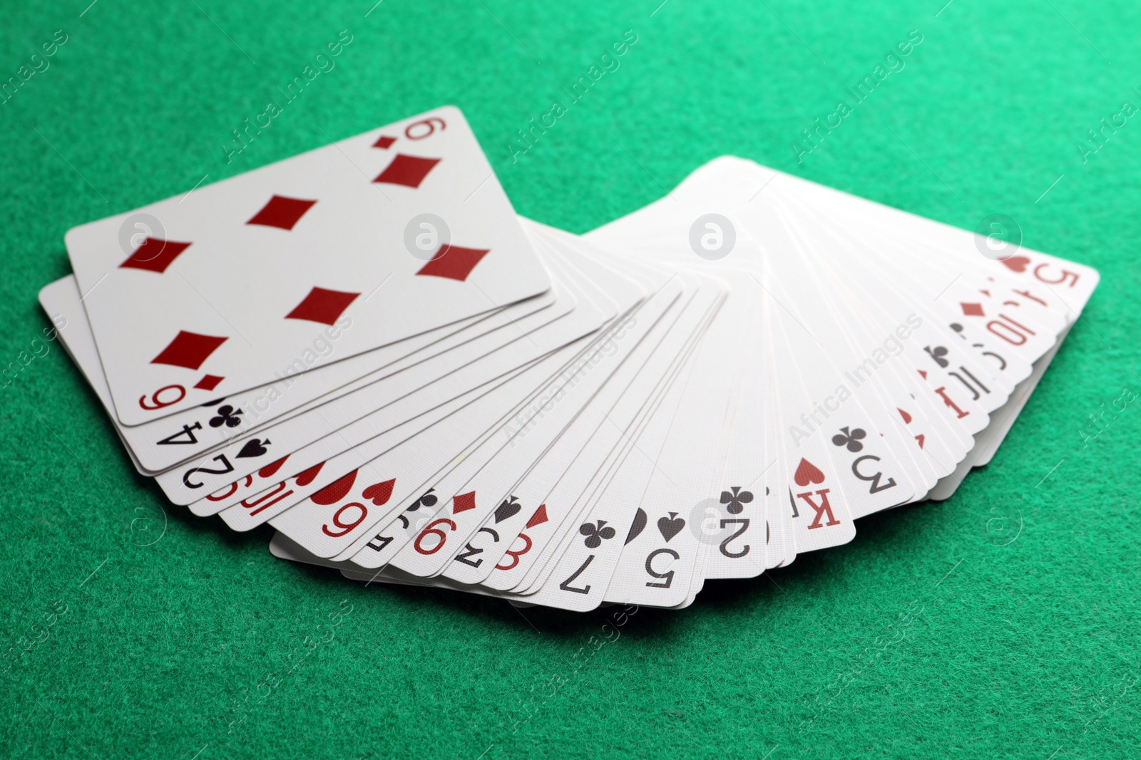 Photo of Fan of playing cards on green table, closeup. Poker game