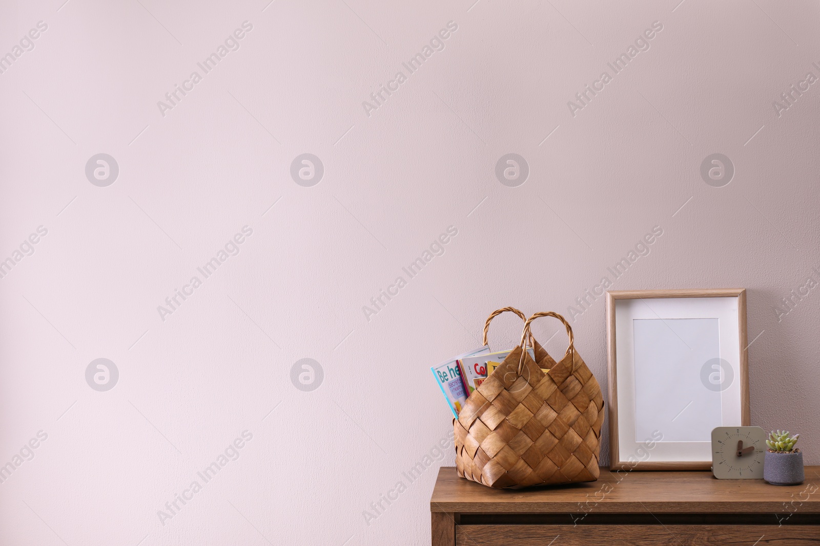 Photo of Wooden chest of drawers with stylish bag, decor and empty frame near light wall in room, space for text. Interior design