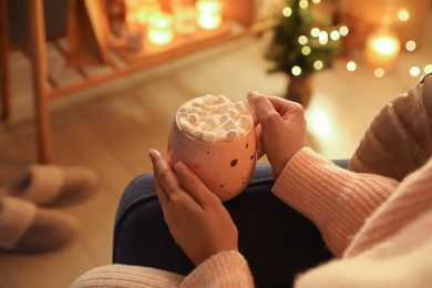 Photo of Woman holding cup of hot drink with marshmallows at home, closeup. Magic Christmas atmosphere