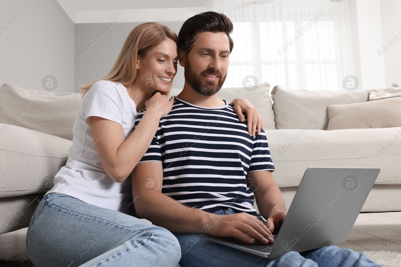 Photo of Happy couple with laptop on floor at home