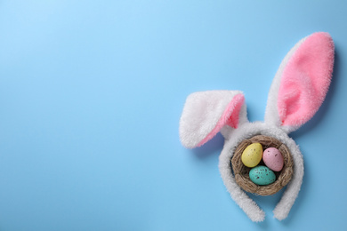 Headband with bunny ears, painted eggs and space for text on light blue background, flat lay. Easter holiday