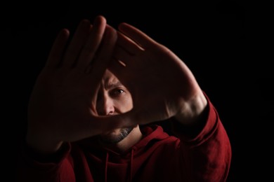 Man showing stop gesture against black background, focus on hands