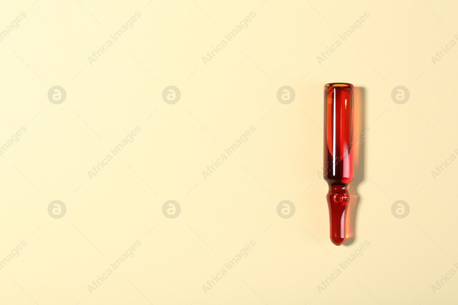 Photo of Glass ampoule with liquid on beige background, top view. Space for text