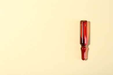 Photo of Glass ampoule with liquid on beige background, top view. Space for text