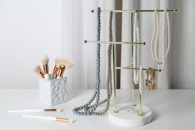 Photo of Interior element. Holder with set of luxurious jewelry and makeup brushes on white dressing table
