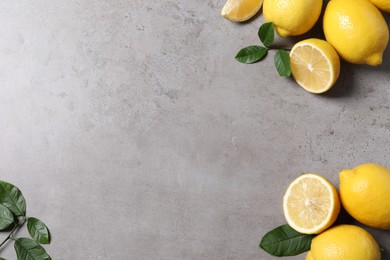 Fresh lemons and green leaves on grey table, flat lay. Space for text