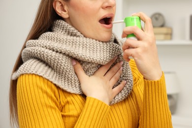 Photo of Adult woman with scarf using throat spray at home, closeup