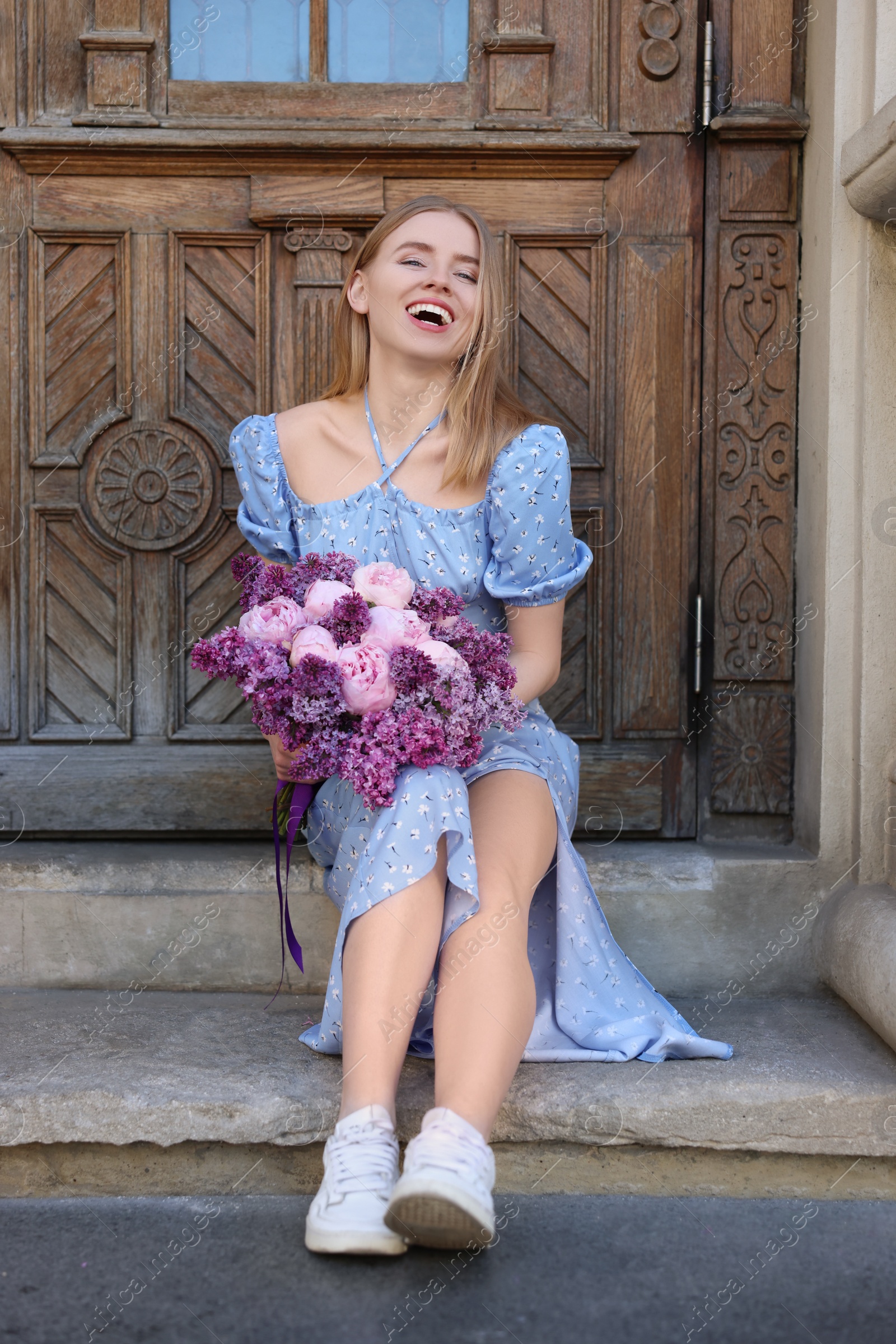 Photo of Beautiful woman with bouquet of spring flowers near building outdoors