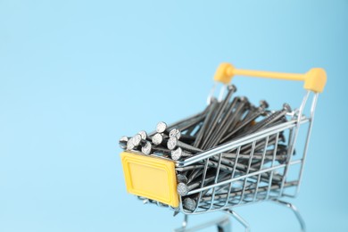 Photo of Metal nails in shopping cart on light blue background, closeup. Space for text