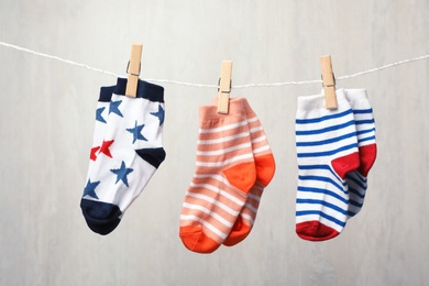 Different child socks on laundry line against light background