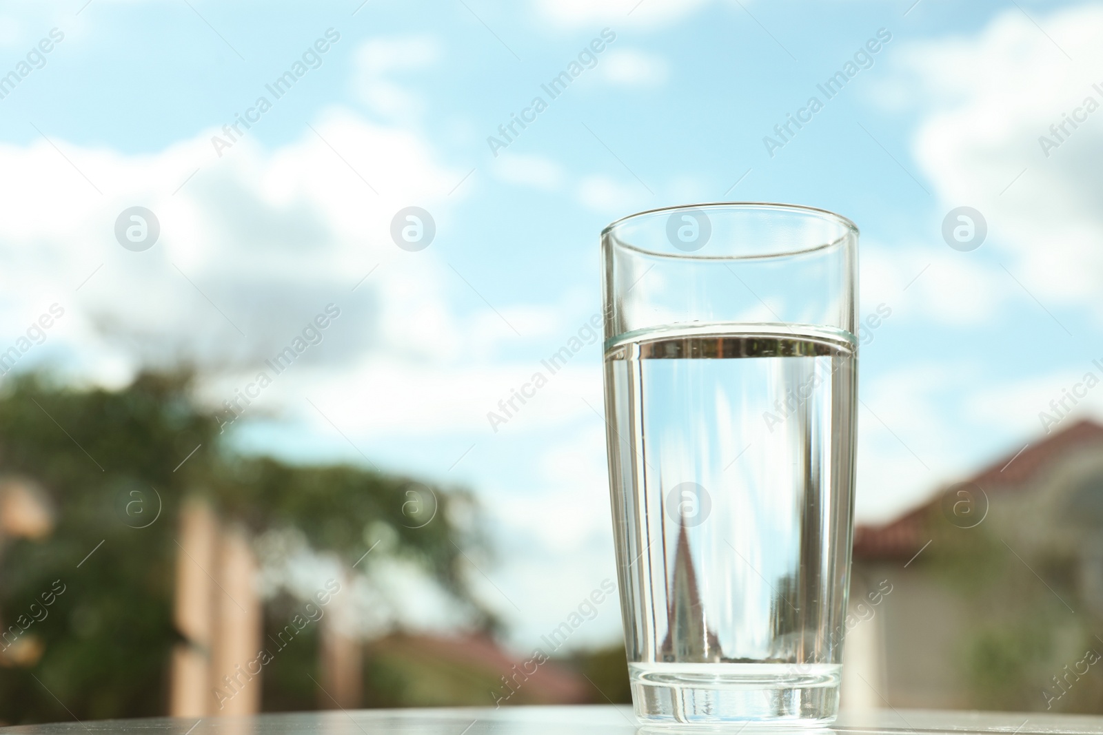 Photo of Glass of fresh water against blurred background outdoors. Space for text