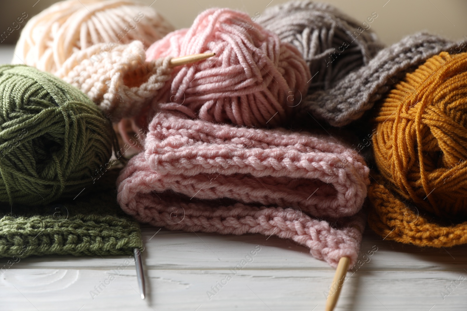 Photo of Balls of soft yarns, knitting and needles on white wooden table, closeup