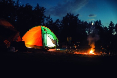 Photo of Glowing camping tent near bonfire in wilderness at night
