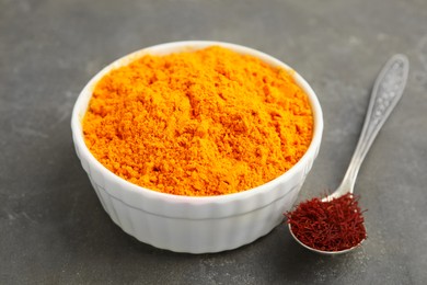 Photo of Bowl of saffron powder and spoon with dried flower stigmas on grey table