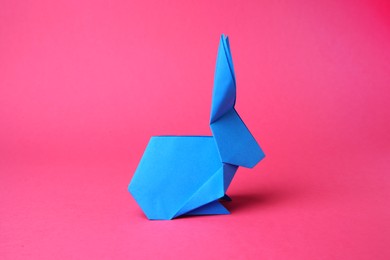 Photo of Light blue paper bunny on pink background. Origami art