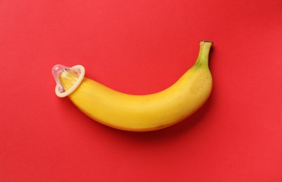 Photo of Banana with condom on red background, top view. Safe sex concept