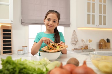 Photo of Little girl with cutting board and knife scraping  vegetable peels into bowl in kitchen