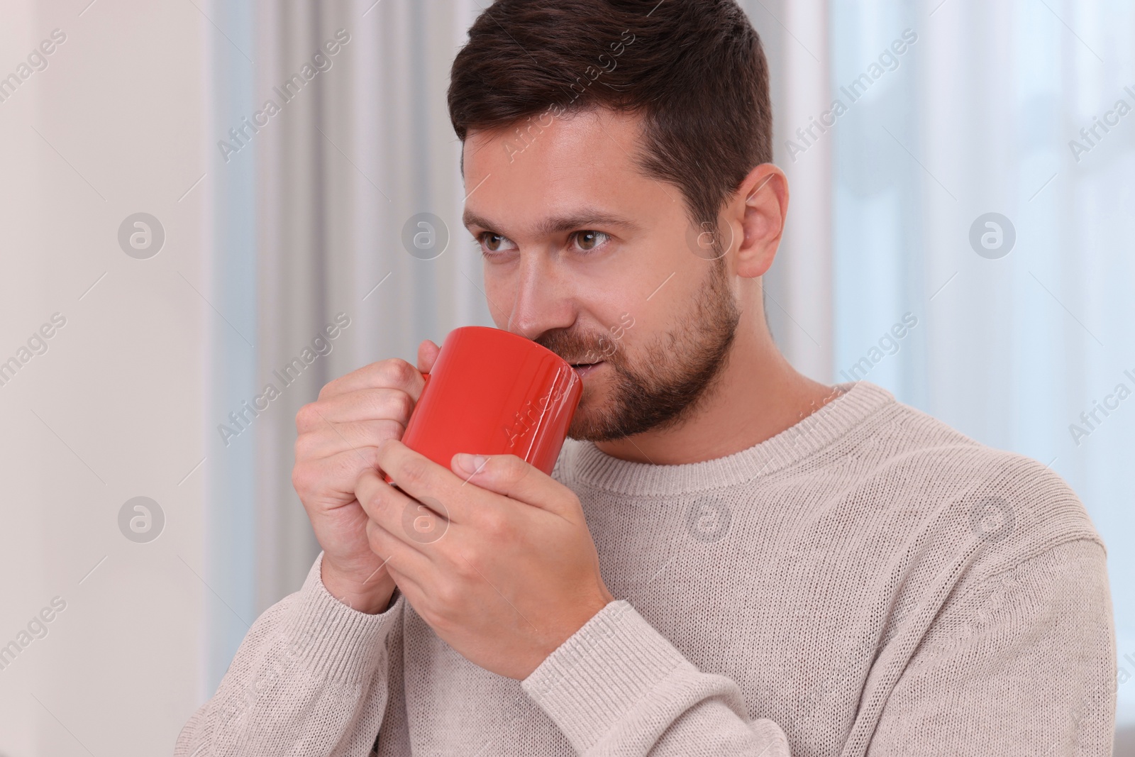 Photo of Man drinking from red mug at home