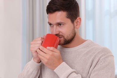 Man drinking from red mug at home