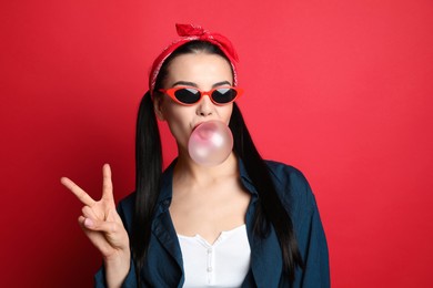 Photo of Fashionable young woman in pin up outfit blowing bubblegum on red background