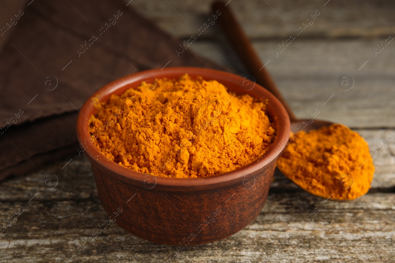 Photo of Bowl and spoon with saffron powder on wooden table, closeup