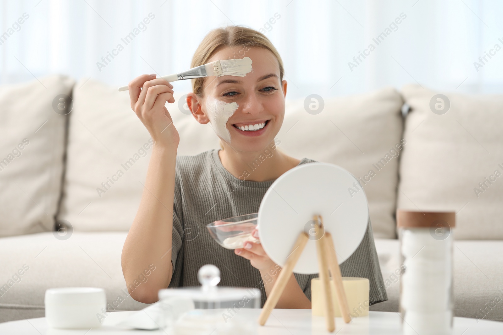 Photo of Young woman applying face mask in front of mirror at home. Spa treatments