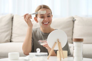 Young woman applying face mask in front of mirror at home. Spa treatments