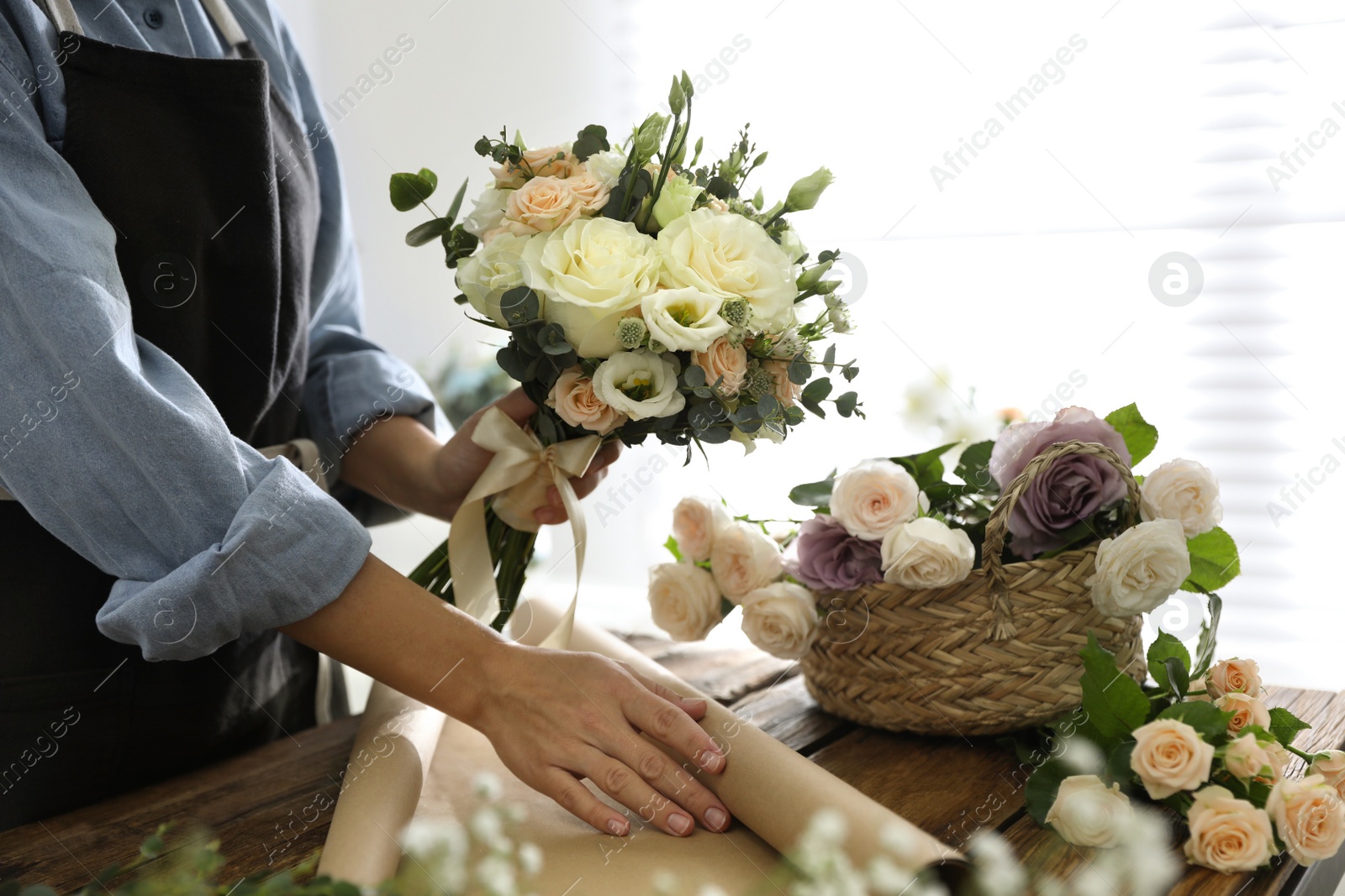 Photo of Florist making beautiful wedding bouquet at wooden table, closeup