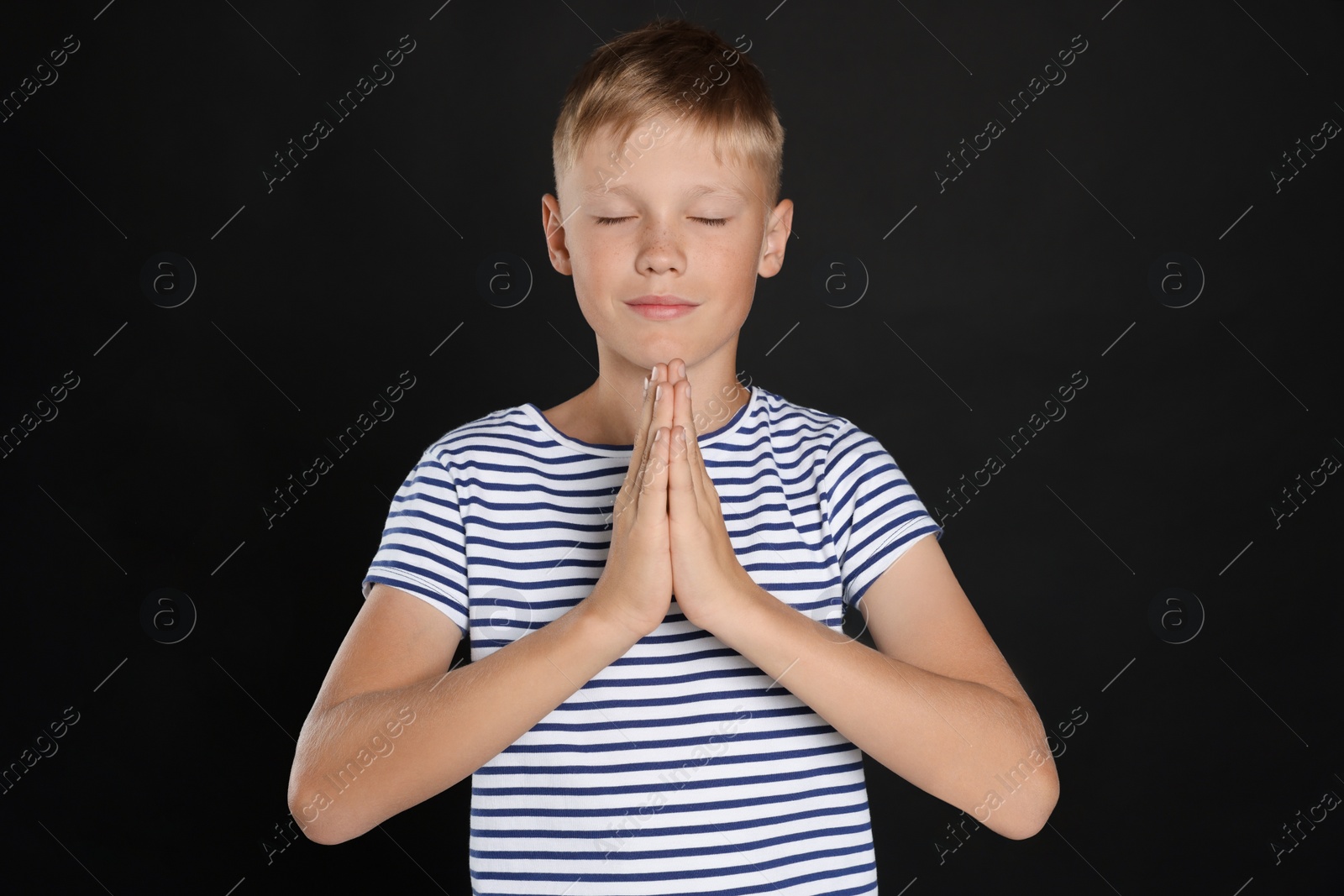 Photo of Boy with clasped hands praying on black background