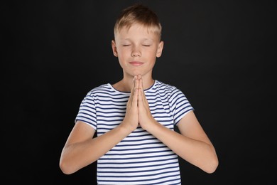 Boy with clasped hands praying on black background