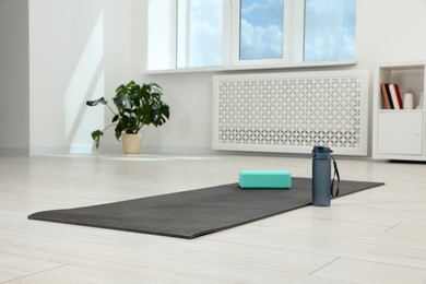 Exercise mat, yoga block and bottle of water on floor in room