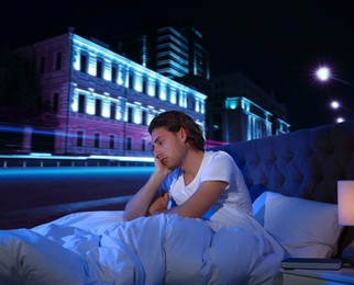 Man in bed and beautiful view of night cityscape on background. Poor sleep because of urban noise