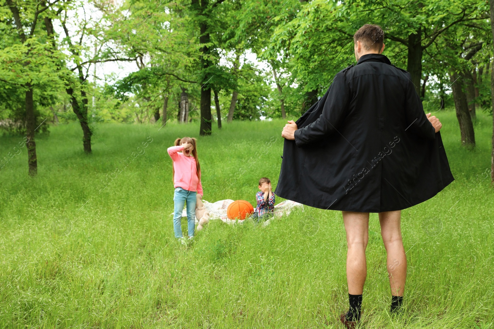 Photo of Male exhibitionist opening his coat in front of kids outdoors. Child in danger