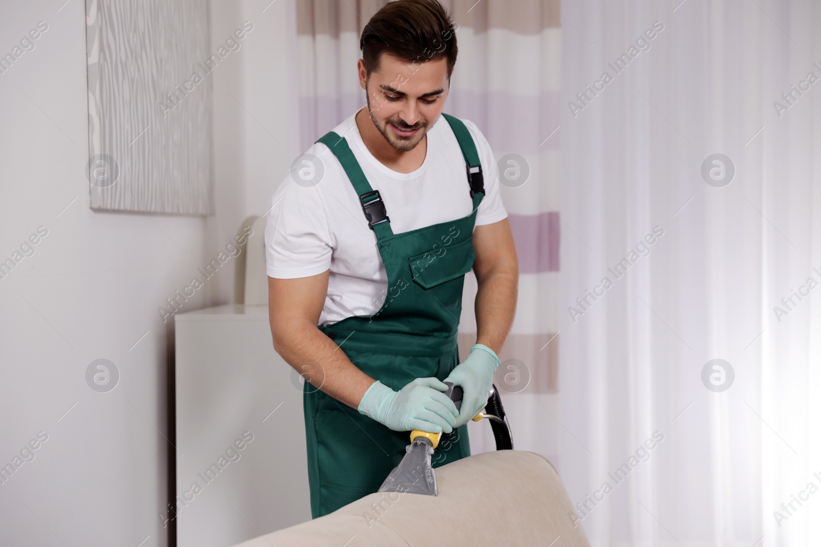 Photo of Professional janitor cleaning sofa in living room