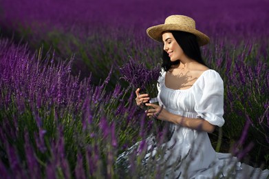 Photo of Beautiful young woman with bouquet sitting in lavender field