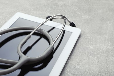 Photo of Computer tablet with stethoscope on grey table, closeup. Space for text