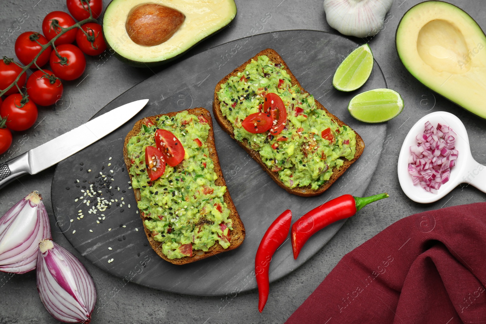 Photo of Slices of bread with tasty guacamole and ingredients on grey table, flat lay