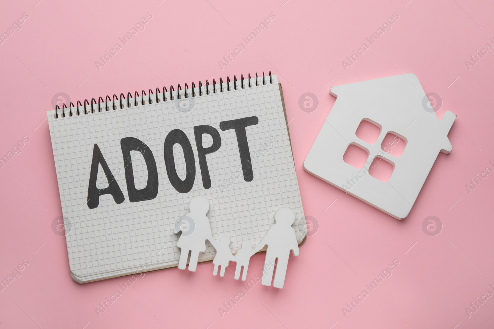 Photo of Family figure, house and notebook with word Adopt on pink background, flat lay