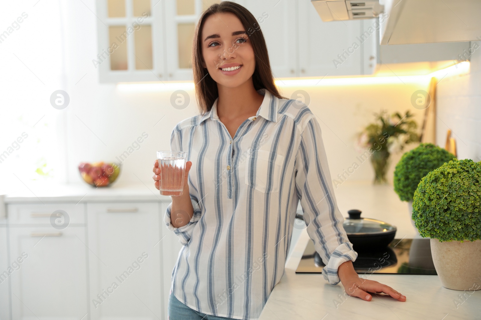 Photo of Young woman holding glass of pure water near countertop in kitchen