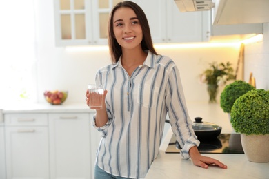 Photo of Young woman holding glass of pure water near countertop in kitchen