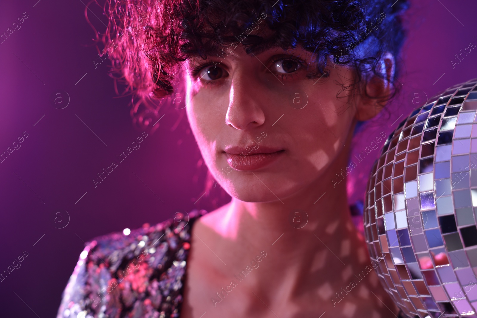 Photo of Beautiful young woman with disco ball posing on color background in neon lights, closeup