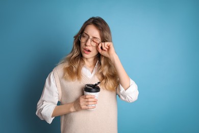 Young tired woman with mug of drink yawning on light blue background