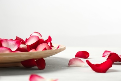 Wooden plate with rose petals on table against white background. Space for text